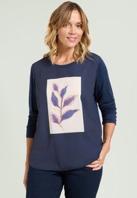 Marineblauwe langslavige top met een bloemenpatroon en paarse bladeren op een crèmekleurige achtergrond. Zachte stof met een ontspannen fit en ronde hals.