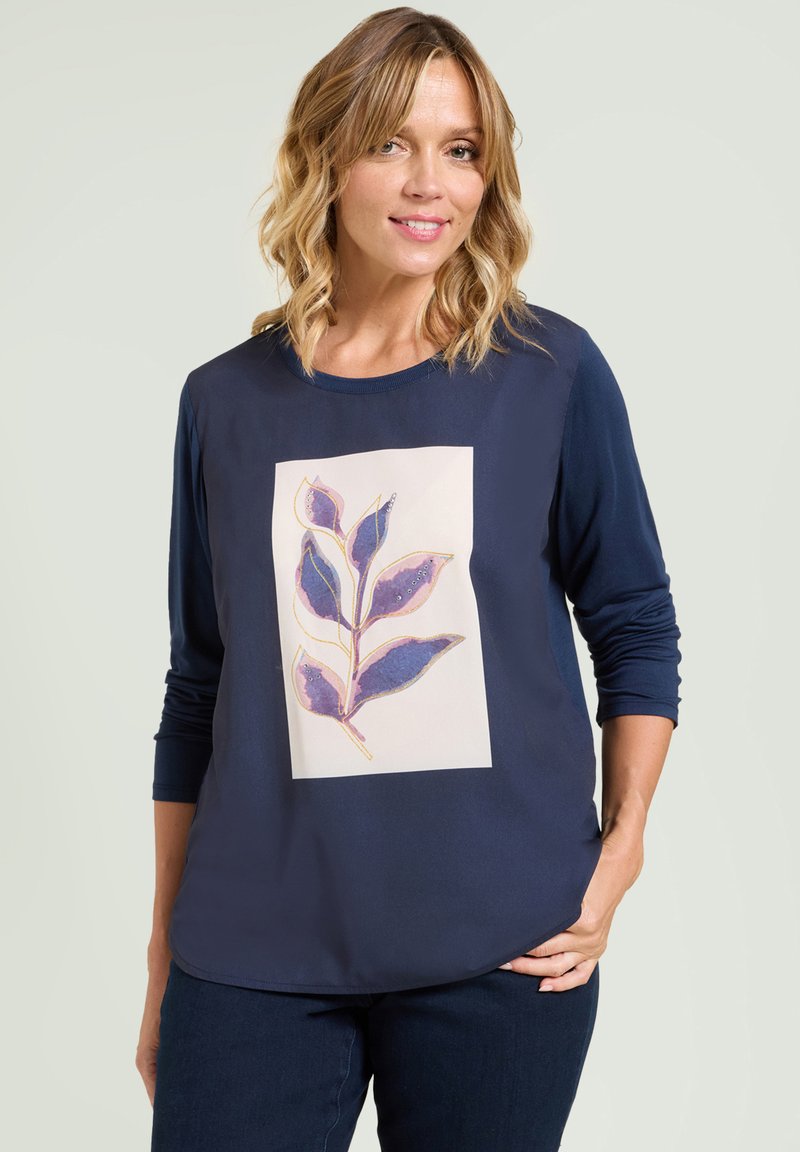 Marineblauwe langslavige top met een bloemenpatroon en paarse bladeren op een crèmekleurige achtergrond. Zachte stof met een ontspannen fit en ronde hals.