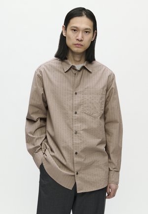 Brown striped button-up shirt with a collar, single chest pocket, and gray undershirt. Model wears dark trousers and has long straight hair.