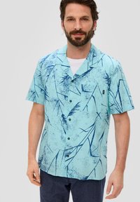 Camisa de manga corta, de color azul claro, con un patrón de hojas en azul oscuro, diseño abotonado, cuello con solapa y un pequeño bolsillo en el pecho.