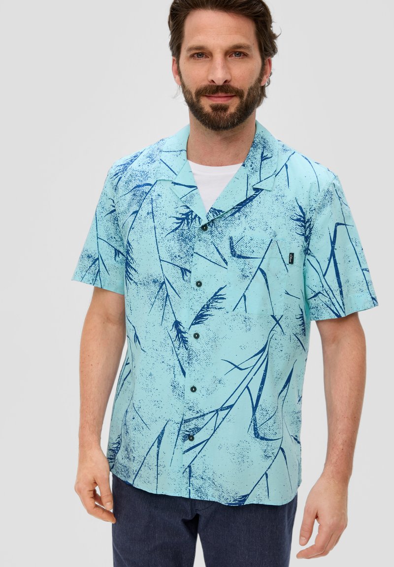 Camisa de manga corta, de color azul claro, con un patrón de hojas en azul oscuro, diseño abotonado, cuello con solapa y un pequeño bolsillo en el pecho.