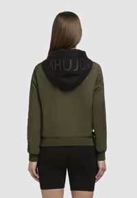 Olijfgroene bomberjack met zwarte capuchon, met een verhoogd logo op de achterkant, elastische manchetten en een gladde textuur.