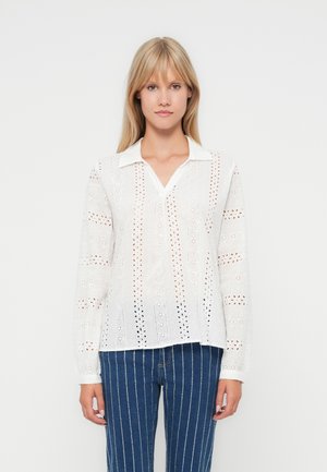 White long-sleeve blouse featuring broderie anglaise design, with a pointed collar and V-neckline. Textured fabric and relaxed fit.