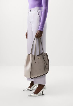 Borsa tote in pelle beige con motivo impresso, due manici e un'etichetta removibile. Abbinata a pantaloni viola chiaro e tacchi argento metallici.