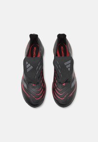 Baskets noires avec des rayures rouges, présentant un dessus texturé, un col rembourré et un design élégant et aérodynamique.
