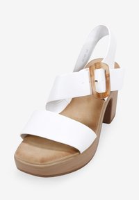 Sandalia de plataforma blanca de piel con dos correas anchas, un acento de hebilla transparente y un tacón de madera clara. Textura suave y diseño de parte posterior abierta.