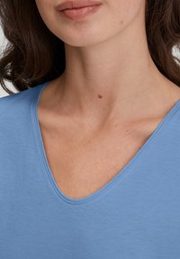 Hellblaues Baumwoll-Shirt mit V-Ausschnitt und kurzen Ärmeln, mit glatter Textur und genähtem Kragen, das eine lockere Passform zeigt.