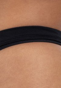 Ceinture élastique noire d'un vêtement, contrastant avec une peau lisse et bronzée, montrant un gros plan sur la texture et la couleur du tissu.