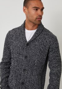 Cardigan a maglia texture in grigio scuro e nero. Caratterizzato da un colletto a scialle, cinque bottoni e dettagli a coste lungo il corpo e le maniche.