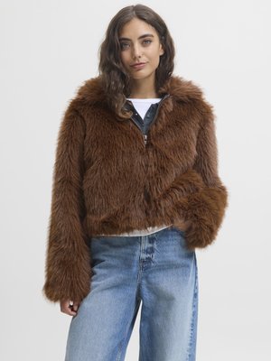 Ruda dirbtinė kailinė striukė su kapišonu, trumpa, plačiomis rankovėmis, derinama su pilku marškinėliu ir šviesiai mėlynomis aukštai juosmeninėmis džinsomis.