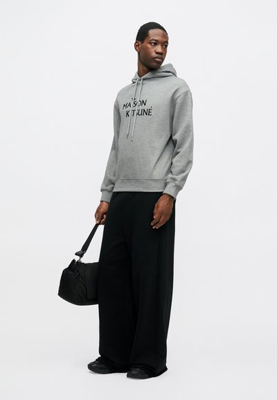 Hanorac gri cu logo "MAISON KITSUNÉ", cu șnur și tiv ribbed; asortat cu pantaloni largi negri și o geantă neagră. Adidași negri completează look-ul.