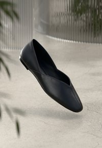 Schwarze Leder-Ballettschuhe mit einer spitzen Spitze und einem V-förmigen Ausschnitt im Obermaterial. Glatte Textur und minimalistisches Design mit einem schlanken Absatz.