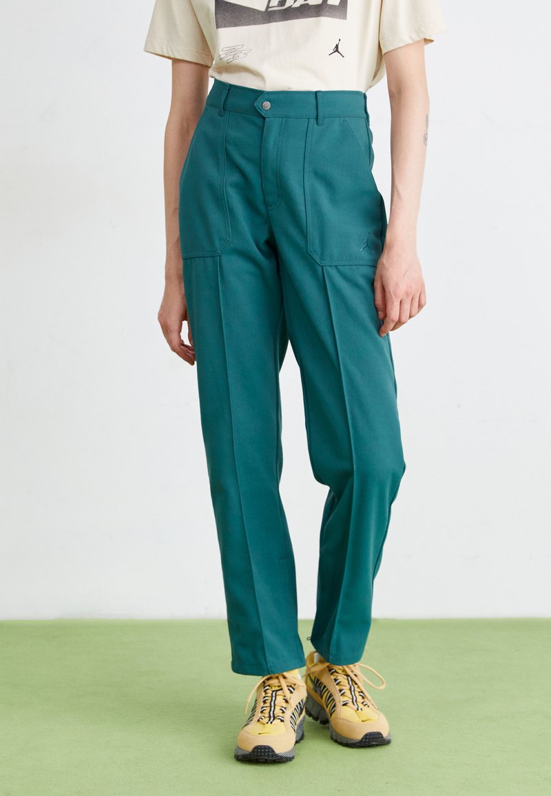 Teal bukser med højt talje, brede ben og forlommer. Kombineret med gule sneakers med sorte accenter og et mønstret sål.