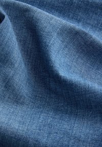 Gros plan sur un tissu en denim bleu doux et texturé avec un tissage visible et des plis naturels créant des ombres et des reflets.
