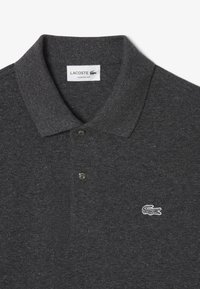 Polo grigio realizzato in tessuto strutturato, con colletto classico, due bottoni neri e un piccolo logo Lacoste bianco sul petto.