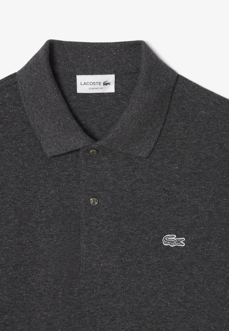 Polo gris en tissu texturé, doté d'un col classique, de deux boutons noirs et d'un petit logo Lacoste blanc sur la poitrine.