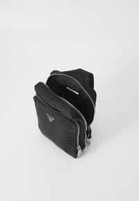 Mochila negra de nailon con varios compartimentos con cremallera, acento de logotipo triangular y textura suave; cuenta con un resistente herraje plateado.