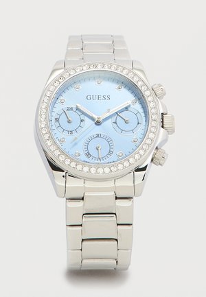 Zilverkleurige metalen armbandhorloge met lichtblauwe wijzerplaat, kristallen uurmarkeringen, drie subwijzerplaten en een met kristallen bezette lunette, merknaam Guess.