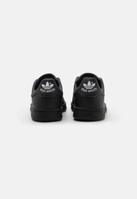 Baskets Stan Smith en cuir noir avec une finition lisse, arborant un logo blanc à l'arrière et une semelle en caoutchouc noir texturée.