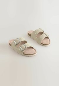 Helle beige Sandalen mit zwei verstellbaren Riemen, silbernen Schnallen und herzförmigen Nieten. Fußbett aus Korkoptik mit strukturiertem Gummisohle.