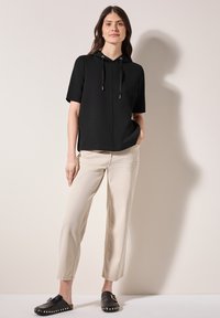 Sudadera negra de manga corta con cordones ajustables, combinada con pantalones beiges de corte holgado y zapatos negros tipo zueco con tachuelas decorativas.