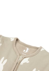 Couverture en coton beige présentant des imprimés de lapins blancs, un col rond et une fermeture éclair à l'avant. L'étiquette indique la taille 70 cm. Texture lisse.