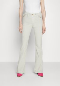 Hellgraue, ausgestellte Jeans aus glattem Material, mit Taschen und einer vorderen Knopfschließe. Kombiniert mit leuchtend pinken Absatzstiefeln.