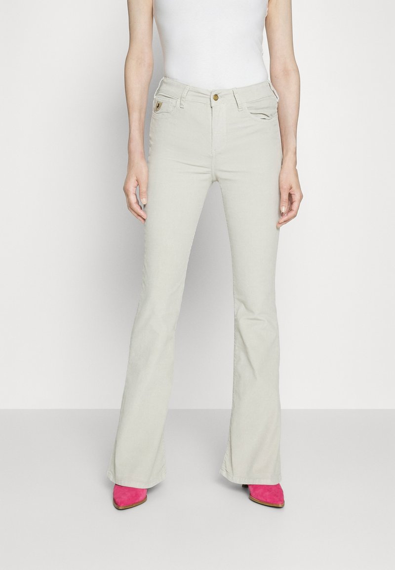 Hellgraue, ausgestellte Jeans aus glattem Material, mit Taschen und einer vorderen Knopfschließe. Kombiniert mit leuchtend pinken Absatzstiefeln.