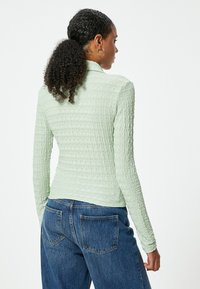Lys grøn, tekstureret langærmet bluse med en tætsiddende design, parret med høj talje blå denimjeans med baglommer.