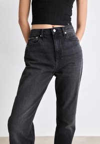 Black denim jeans with a high waist, straight leg cut, and front pockets. Features sturdy stitching and metal hardware accents.