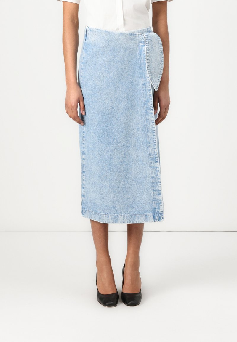 Lyseblå denim midi-skjørt med omslagdesign, som har et unikt sidepanel og ren søm. Brukt med svarte høye hæler.