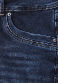 Jeans de mezclilla azul oscuro con un bolsillo frontal, costuras doradas en contraste y un detalle de botón plateado. Textura suave con un ligero desgastado.