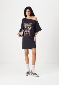 Juoda oversize stiliaus t-shirt su "Vasaros atmosfera" grafika, kurią puošia spalvingas palmės dizainas, derinama su sidabrinėmis bateliais ir baltais kojiniais.