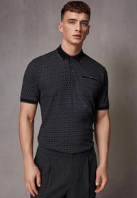 Polo shirt de culoare navy cu un design patterned, mâneci scurte și guler. Include nasturi și un buzunar pe piept pentru un plus de detaliu.