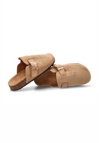 Zuecos de ante en color beige con plantilla de corcho y suela de goma negra. Cuentan con una correa ancha con una hebilla metálica. Superficie texturizada.
