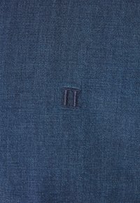 Blue denim fabric with stitched Roman numeral II centered.