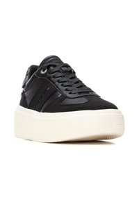 Zapatilla negra con upper de cuero texturizado, cordones planos y una gruesa suela de plataforma blanca. Presenta un branding sutil y ojales reforzados.