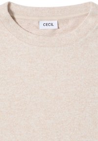 T-shirt en coton beige clair avec un col rond. Présente un motif texturé subtil et une étiquette portant la mention "CECIL" au niveau du cou.