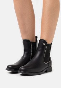 Svarta läderankelstövlar med elastiska sidopaneler, prydda med silverfärgade nitar längs kanterna och platta gummisulor.