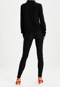 Maglia nera a maniche lunghe con taglio dritto e colletto alto abbinata a jeans neri aderenti e scarpe con tacco rosso.