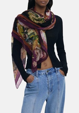 Donna che indossa un cardigan nero a coste con bottoni, jeans a vita alta blu chiaro e una sciarpa multicolore con motivo floreale drappeggiata sulle spalle.