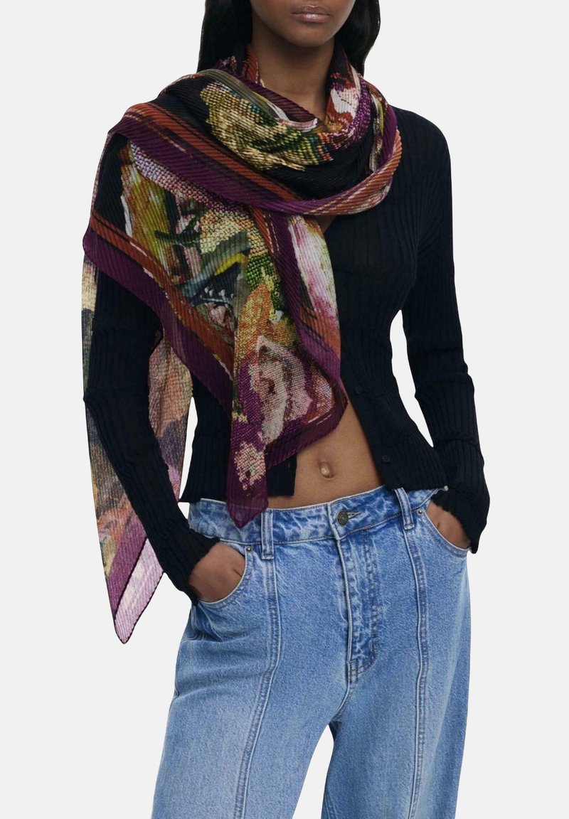 Femme portant un cardigan noir à côtes avec boutons, un jean bleu clair taille haute et une écharpe à motif floral multicolore drapée sur les épaules.