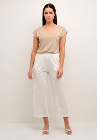 T-shirt beige à col en V avec des manches courtes, associé à un pantalon large écru. Tissu léger avec une texture subtile et des sandales à lanières.