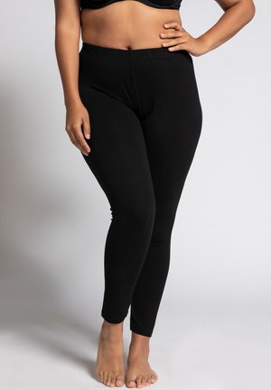 Leggings noirs en tissu extensible avec une taille élastique, ajustés sur toute la jambe, présentant une texture lisse et sans motifs visibles.