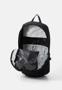 Schwarzer Rucksack mit grauem Innenraum, ausgestattet mit einem oberen Reißverschluss, einem Innenfach und Seitentaschen. Das Material scheint robust mit einer strukturierten Oberfläche zu sein.