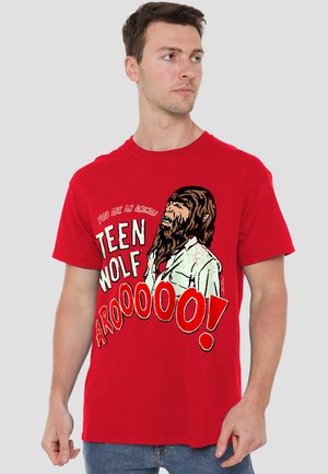 Rotes Baumwoll-T-Shirt mit einem Grafikdruck eines Wolfcharakters in Schwarz und Weiß, mit dem Text "DU BIST EIN TIER! TEEN WOLF AROOOOOO!"