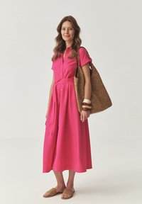 Fuchsialilla, kortærmet skjortekjole med bælte, der har en flydende nederdel. Tilbehør omfatter en vævet tan tote og stablede armbånd.