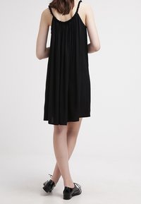 Black sleeveless dress with a gathered back, knee-length, made from lightweight fabric. Worn with matching black shoes, smooth surface texture.