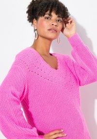 Maglione rosa lavorato a maglia con scollatura a V, vestibilità ampia e maniche a coste. Presenta dettagli in maglia aperta e una finitura testurizzata.