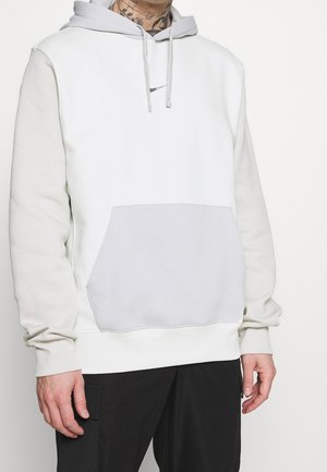 Haut de survêtement gris clair avec poche kangourou, panneaux d'épaule contrastants et capuche à cordon de serrage. Fabriqué en matériau doux. Présente un petit logo.